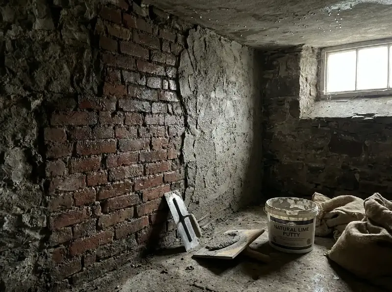 Kalkpleister die op een vochtige oude bakstenen muur in een kelder wordt aangebracht, grove grijze structuur